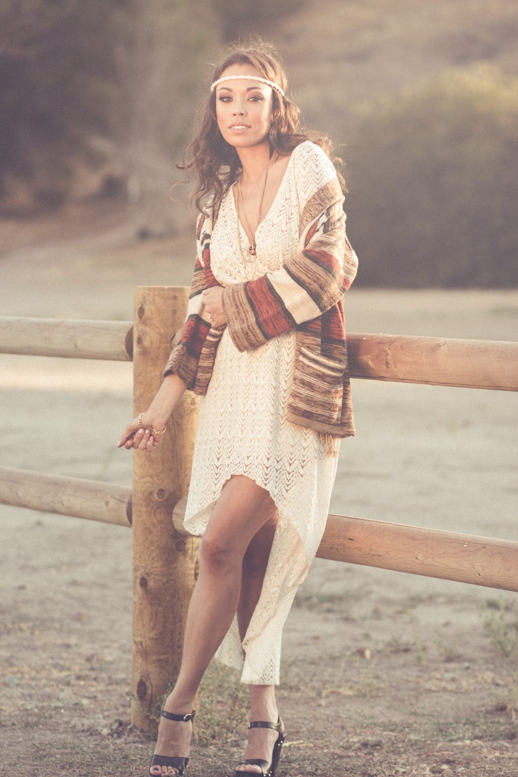 Woman in a bohemian dress leaning on a wooden fence at golden hour